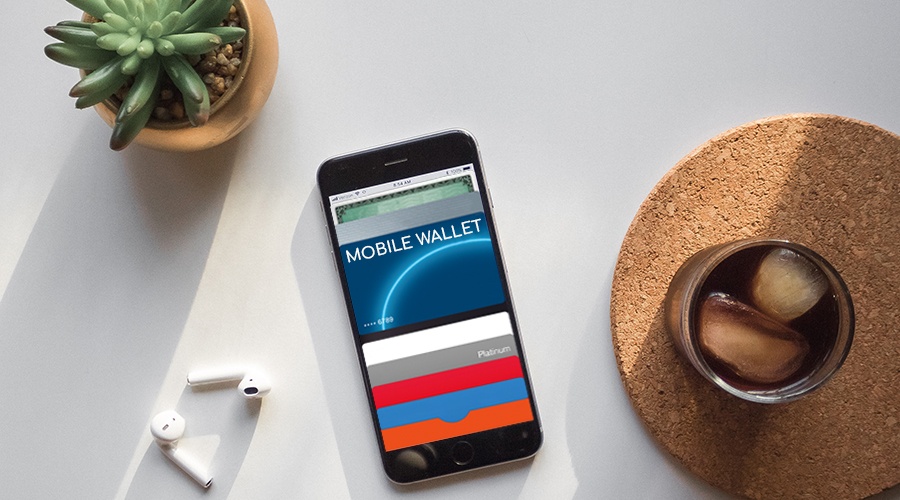 Smartphone with a mobile wallet lying next to a plant, pair of headphones and a glass of iced tea