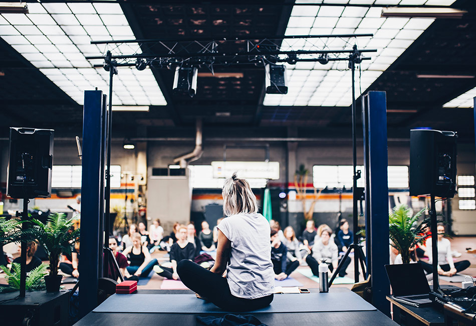 Yoga instructor sitting on stage facing a room full of students